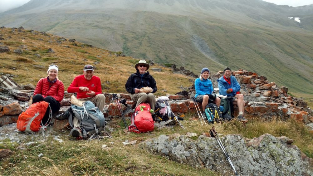 Five people sitting on a low stone wall eating lunch