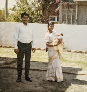 Young Pakistani couple holding a baby. The woman is wearing a sari and the man is wearing slacks and a white shirt