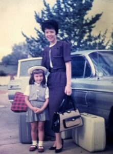 Woman dressed in skirt suit next to a 1957 Chevy with her yound daughter in a pleated skirt, matching top and white hat