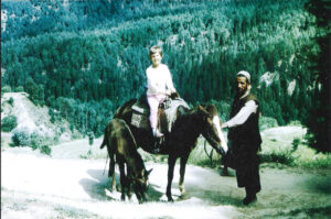 A young girl on a pony with a Kashmiri man with mountainous forest in the background