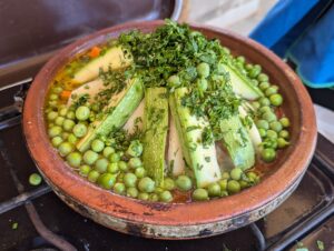 Vegetable tagine showing zucchini and peas topped with parsley in a tagine cooker.