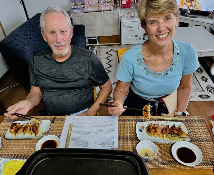 Author and husband seated in a tiny kitchen preparing to eat gyoza with chopsticks