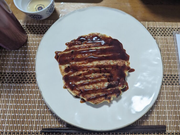 Cooked okonomiyaki (omelette or pancake) with brown sauce drizzled over it in a linear pattern