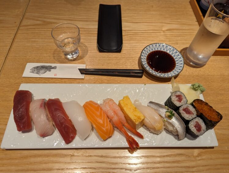 A dozen different types of sushi with a dipping sauce