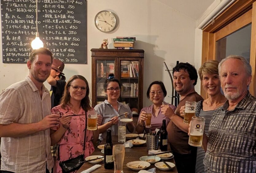 Seven members of a food walking tour group holding mugs of beer and chopsticks for teriyaki chicken