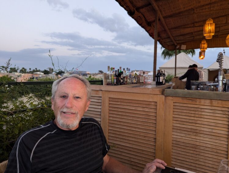 A man seated at a rooftop bar at sunset.