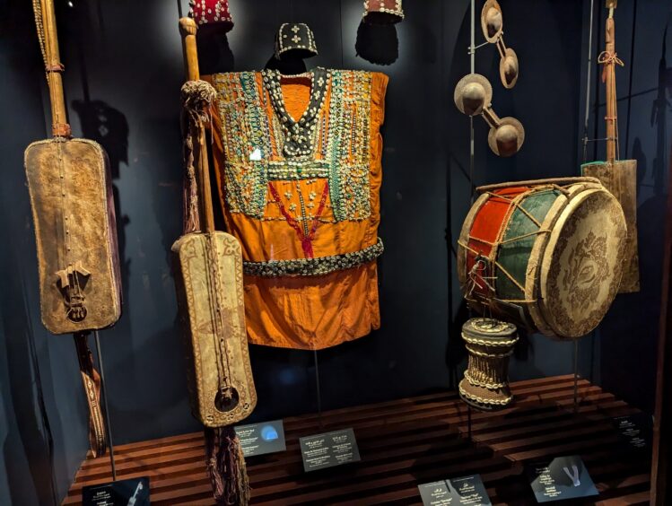 Two stringed instruments and two drums along with a beaded orange vest in a museum display
