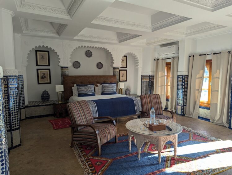 Hotel bedroom with bed and sitting area with two comfortable chairs and round table, descorated with traditional Moroccan fabrics
