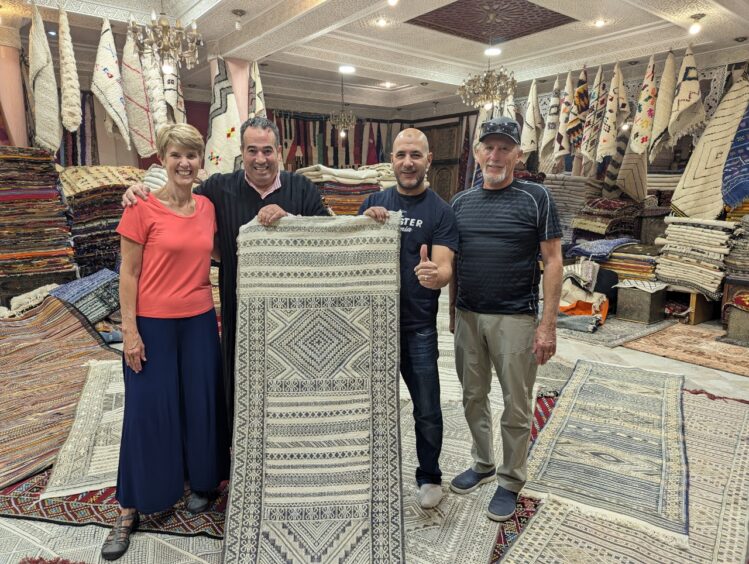 A woman and three men holding a rug