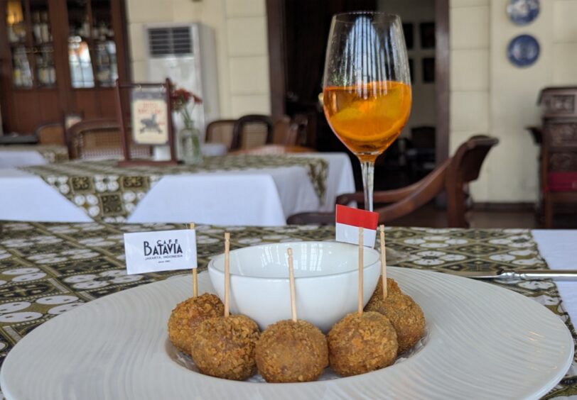 Deep fried balls of meat (bitterballen) are displayed on a plate with toothpicks. A glass of rose is on the table. 