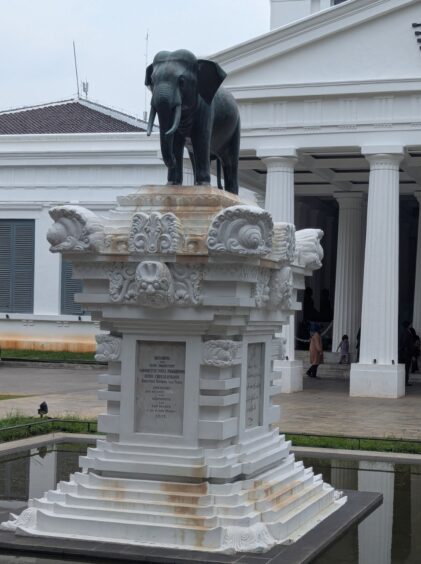 Small elelphant statue atop a large white ornate pedestal. 