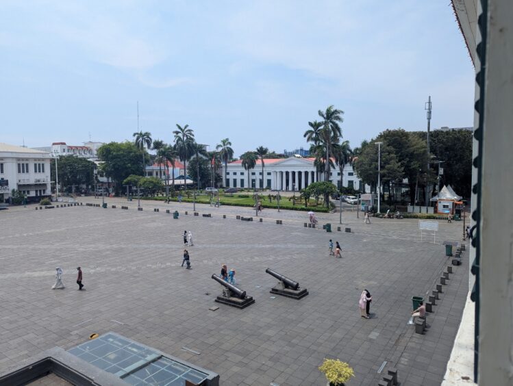 Large square surrounded by colonial style buildings. Two canons are visible. 