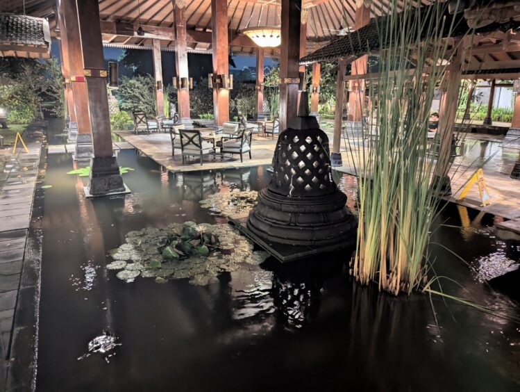 An attractive patio with a replica of a stupa in a pond with reeds and water lilies and outdoor seating.