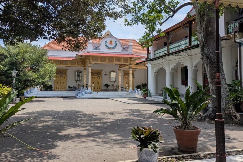 A courtyard in the Sultan's Palace with grand columned entrances to the buildings and much tropical vegetation in the gardens.