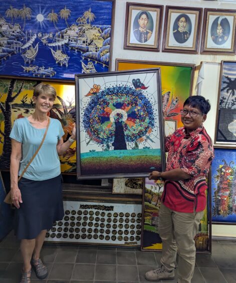 The author and batik artist together are holding the Tree of Life batik art piece in a wooden frame that he created.