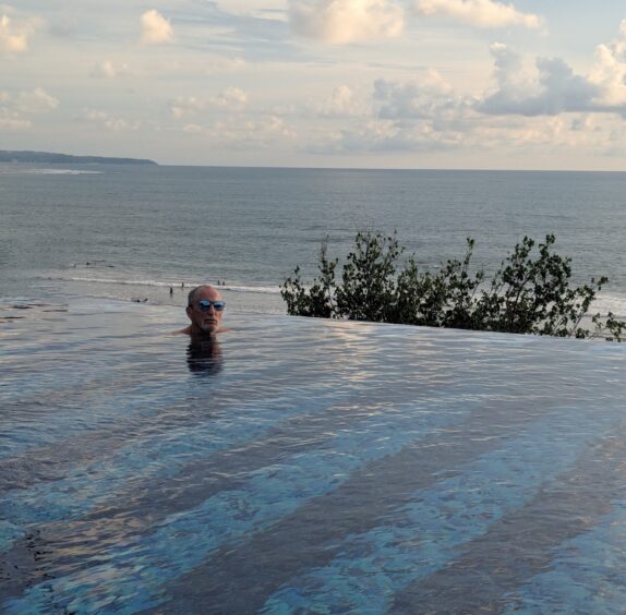 Man sits in infinity pool with the ocean in the background