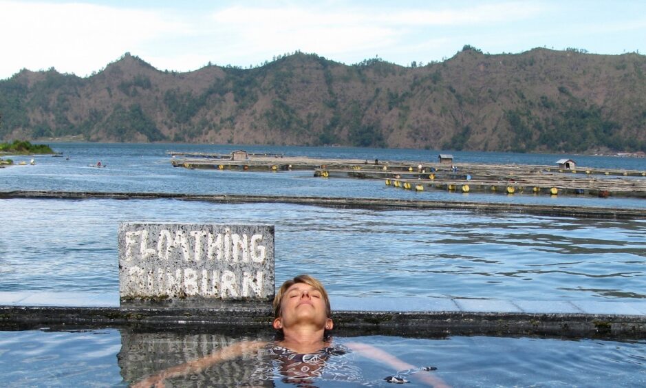 Woman floats in hot springs in front of a sign reading "Floating Sunburn."