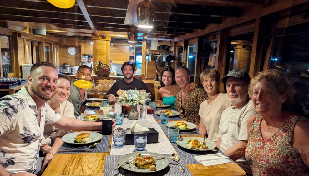 Group of nine guests seated around a wooden table at dinner
