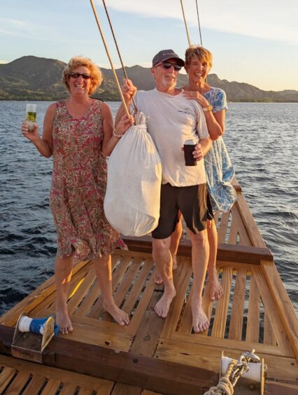 A man and two women with big smiles at the prow of the boat holding drinks