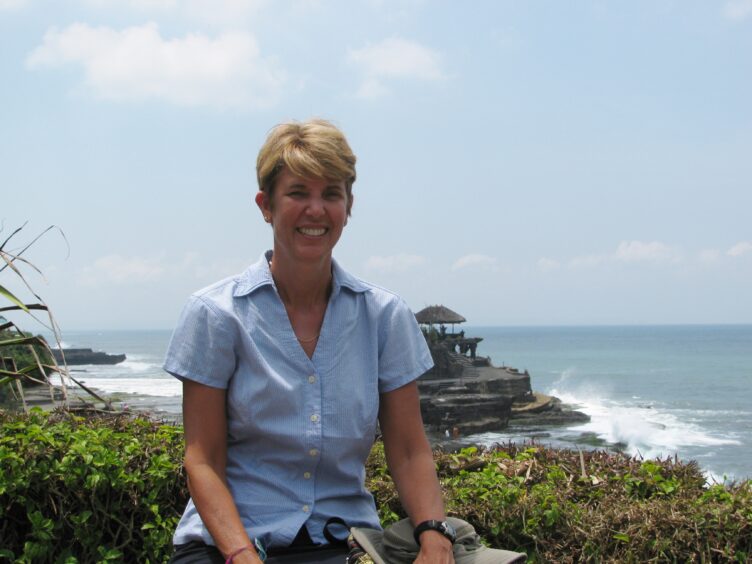 Woman sitting on a wall with Tanah Lot temple in the background in the surf