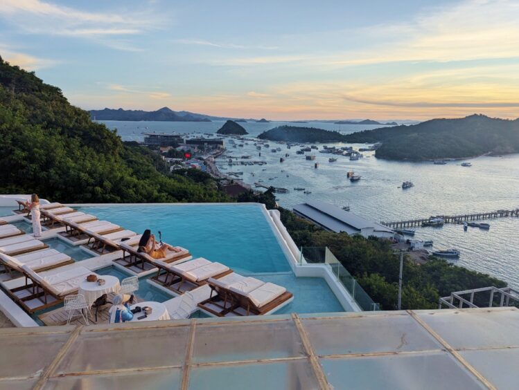 An infinity pool at a hillside hotel with the bay spread out in front, dotted with small boats