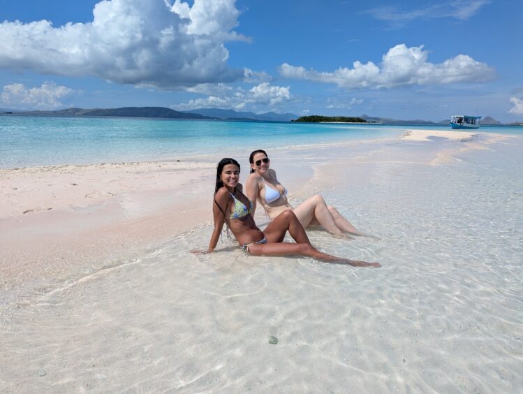 Two women in bikinis posing on a sandbar.