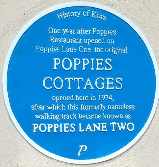 Sky blue sign with information about Poppies Cottages dating from 1974 when the walking track was named Poppies Lane Two.