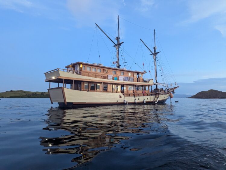 Two masted wooden boat with upper and lower decks against a blue sky