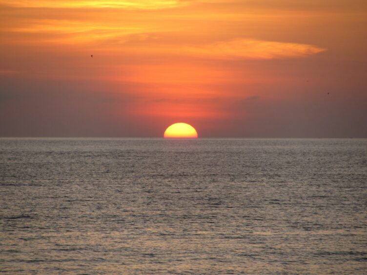 Yellow sun sinking into the horizon against a red-orange sky at Kuta Beach