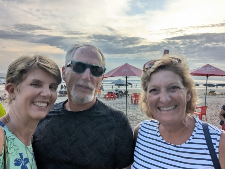 Two women and one man at a beach with beach umbrellas and surf