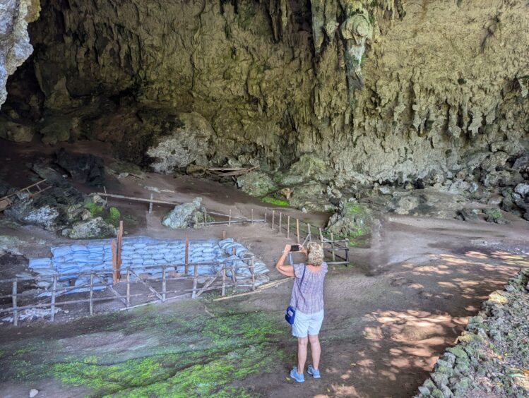 Woman taking a photo of large overhanging cave with sandbag-lined pit